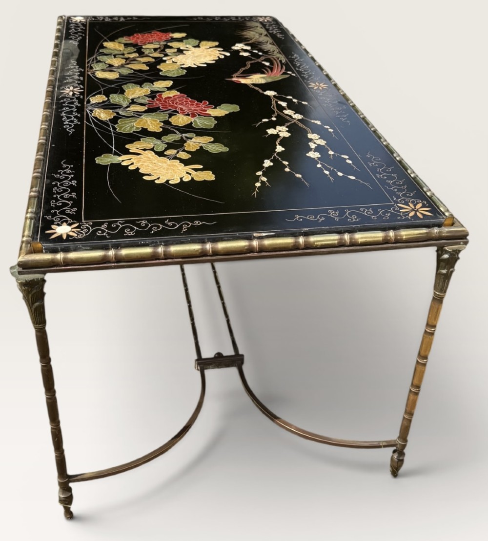 A rectangular mid-century low table featuring a faux-bamboo brass frame, X-form stretchers, and a black lacquered top decorated with colourful Chinoiserie floral patterns.