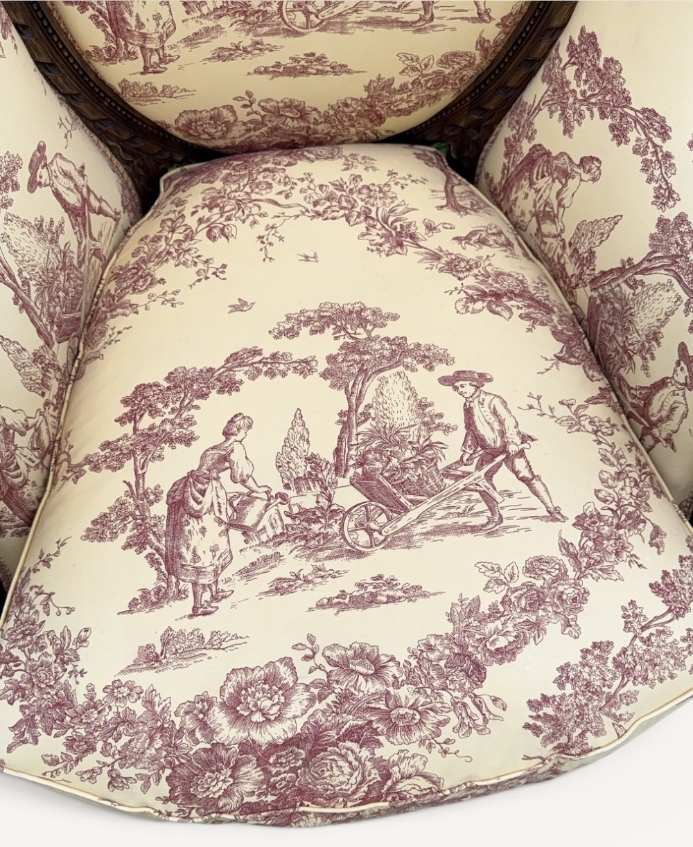A pair of carved wooden French bergere armchairs upholstered in cream and burgundy toile de Jouy patterned fabric. View IV
