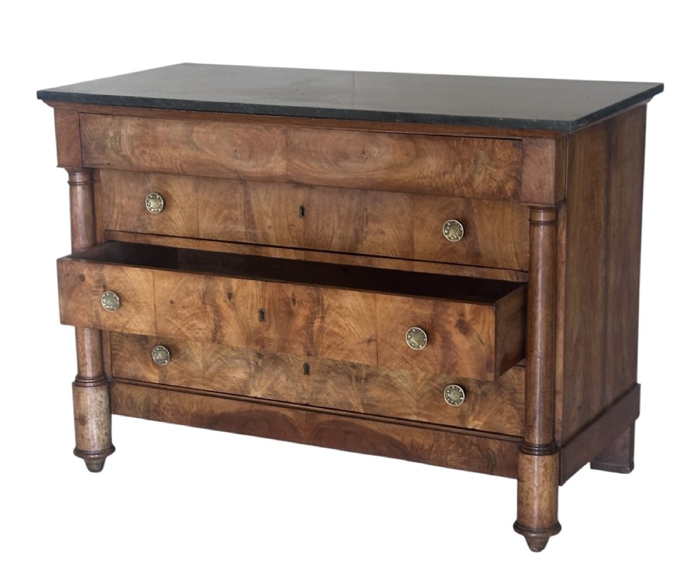 A 19th-century French Charles X walnut commode featuring three lower drawers with round metal pulls, flanked by architectural side columns and topped with a dark marble slab. View V