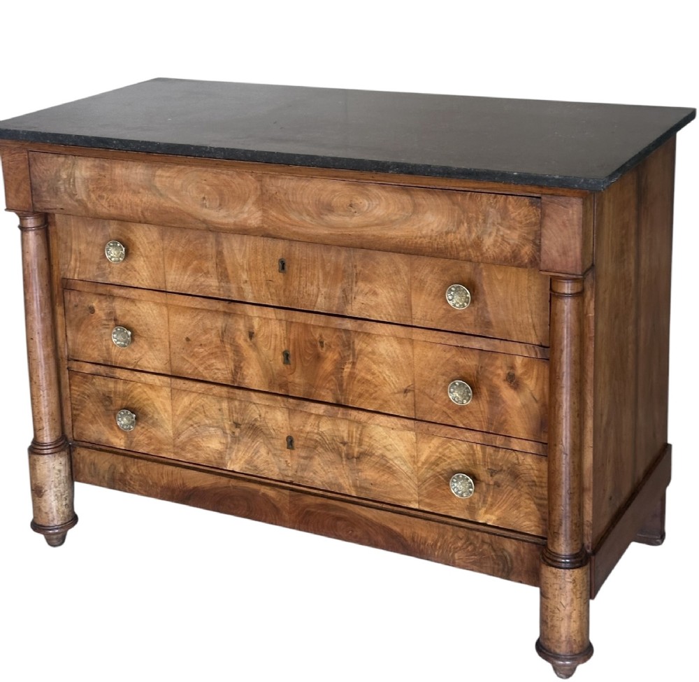 A 19th-century French Charles X walnut commode featuring three lower drawers with round metal pulls, flanked by architectural side columns and topped with a dark marble slab. View VI