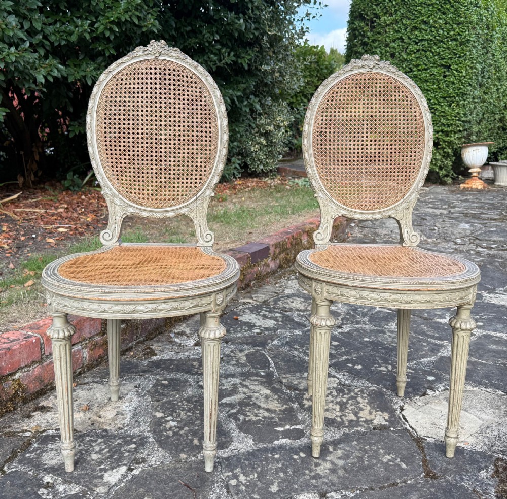 A pair of French Louis XVI style side chairs with oval cane backs, woven cane seats, distressed painted frames, and turned fluted legs. View II
