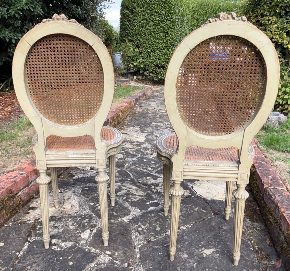 A pair of French Louis XVI style side chairs with oval cane backs, woven cane seats, distressed painted frames, and turned fluted legs. View IV