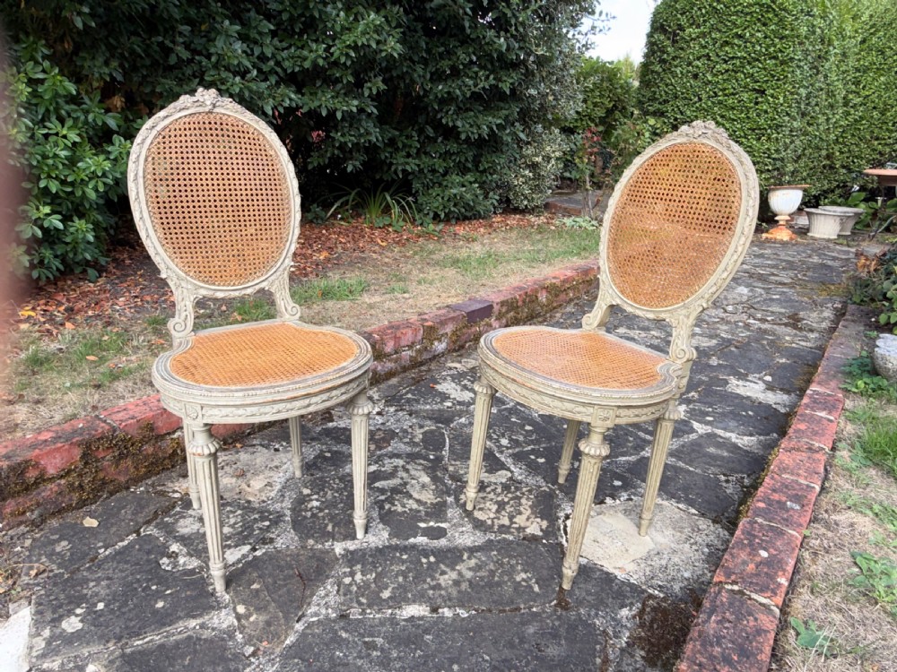 A pair of French Louis XVI style side chairs with oval cane backs, woven cane seats, distressed painted frames, and turned fluted legs. View V