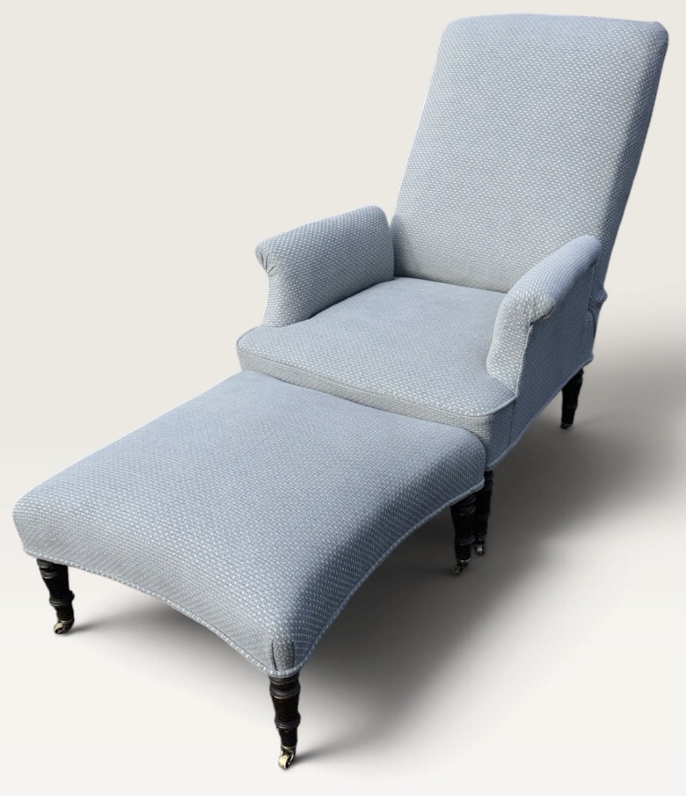 A 19th-century French reclining armchair and matching contoured footstool upholstered in pale blue woven fabric with dark turned wood legs on brass castors.