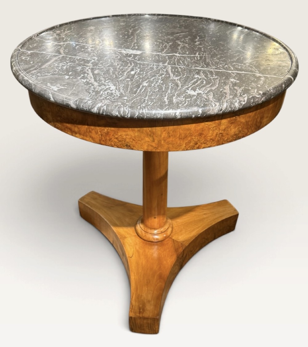 A circular antique centre table featuring a grey veined marble top, burr walnut veneered apron, a central turned column, and a triform platform base. View II