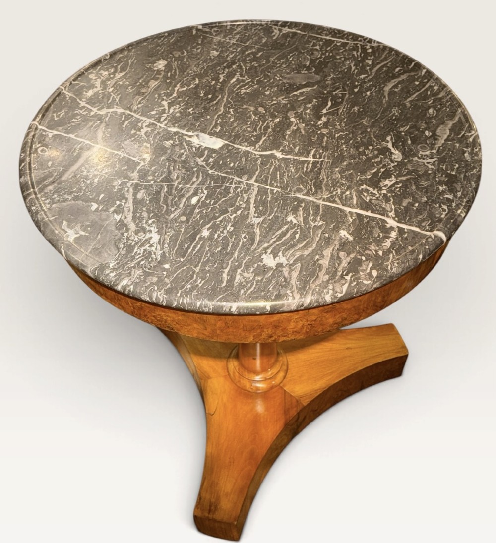 A circular antique centre table featuring a grey veined marble top, burr walnut veneered apron, a central turned column, and a triform platform base. View V