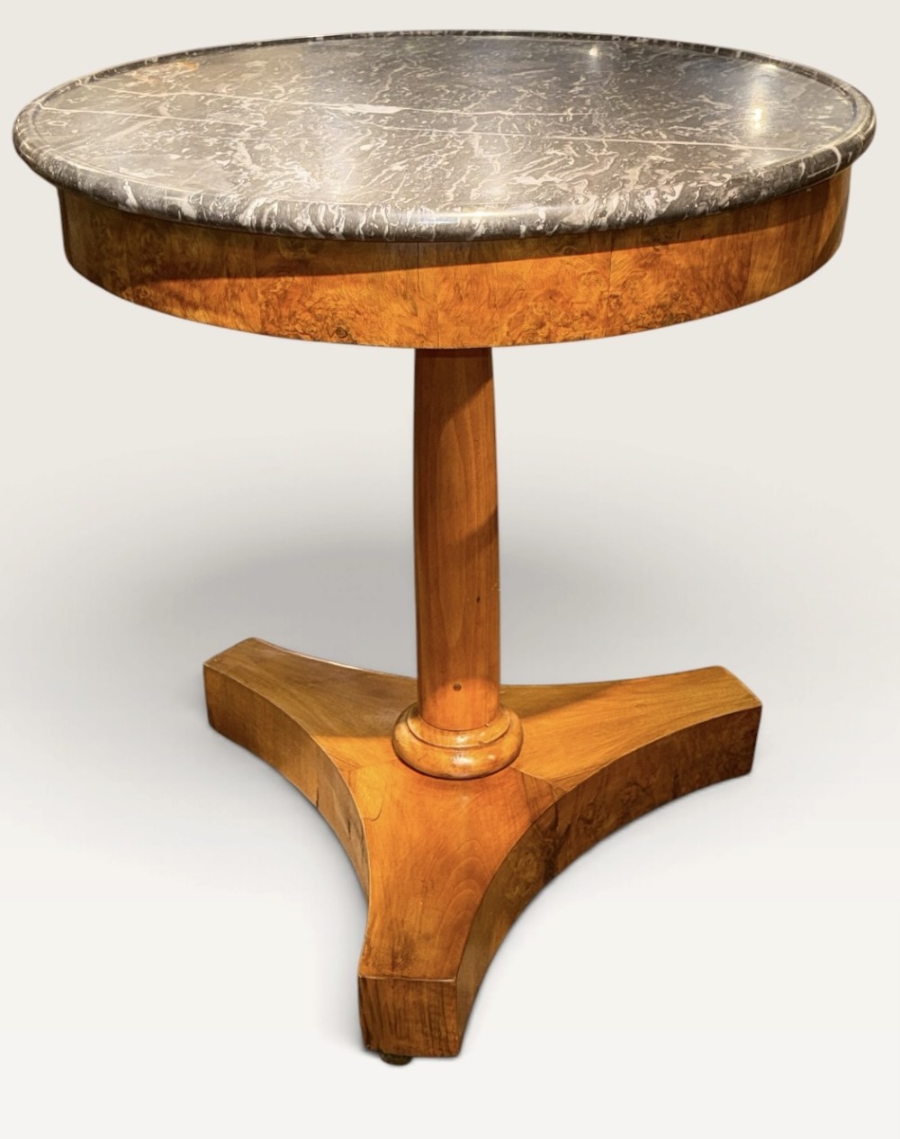 A circular antique centre table featuring a grey veined marble top, burr walnut veneered apron, a central turned column, and a triform platform base. View VI