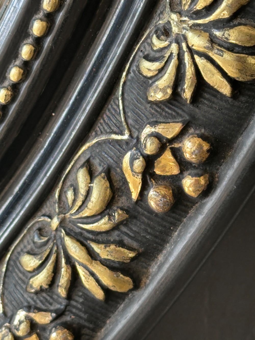 A rectangular black framed mirror with indented corners, gold leaf moulding, and a central oval mirror plate bordered by gilded floral patterns. View III