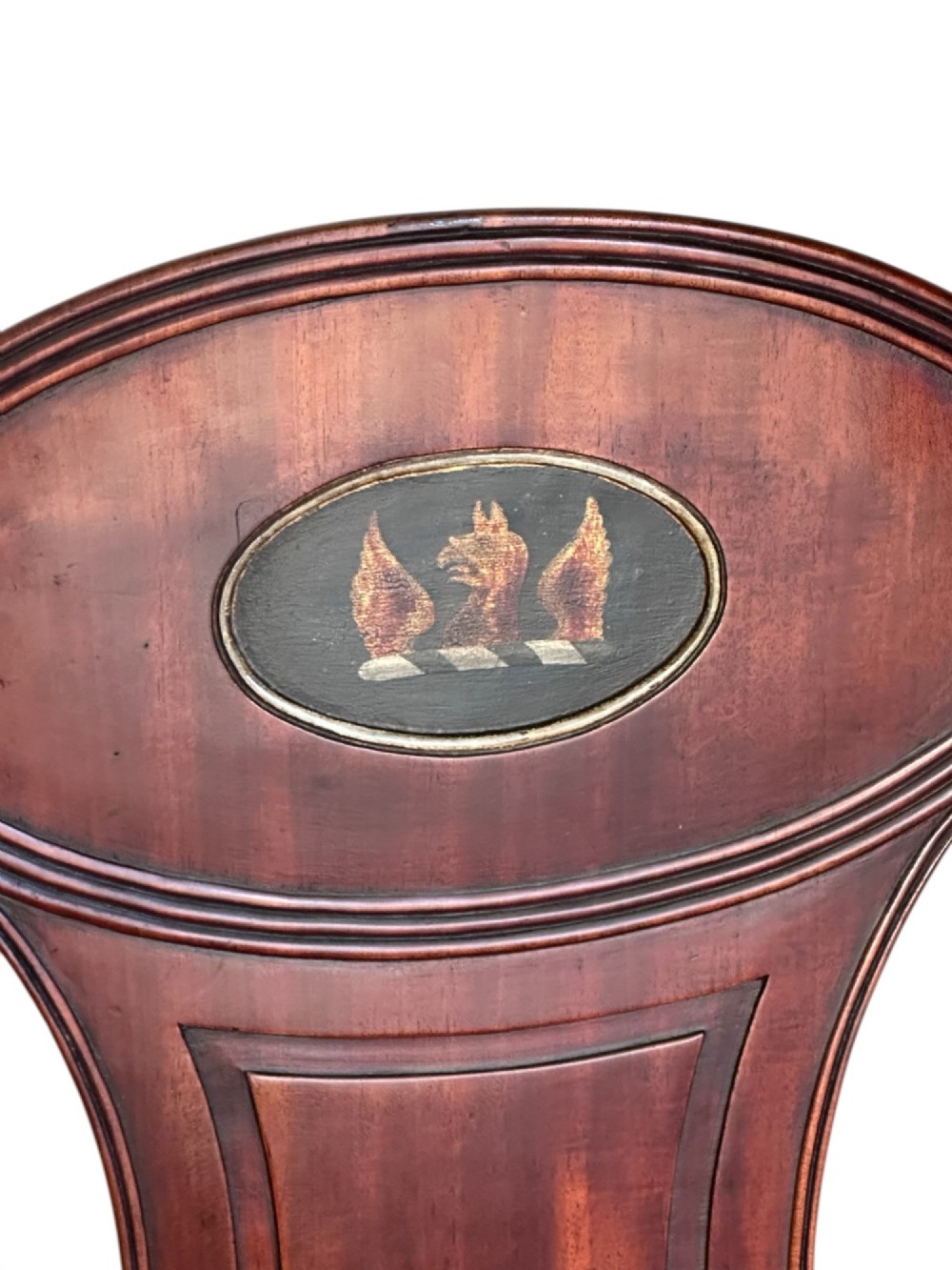 A pair of antique dark mahogany hall chairs featuring oval backrests decorated with painted armorial crest medallions, solid timber seats, and turned front legs. View IV
