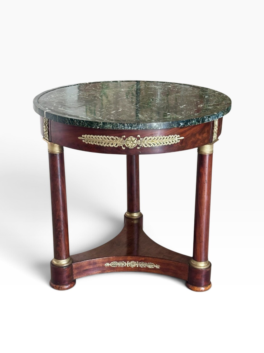 A 19th-century French Empire gueridon centre table featuring a polished circular green marble top, mahogany frame with gilded bronze mounts, three column legs, and a triform base.