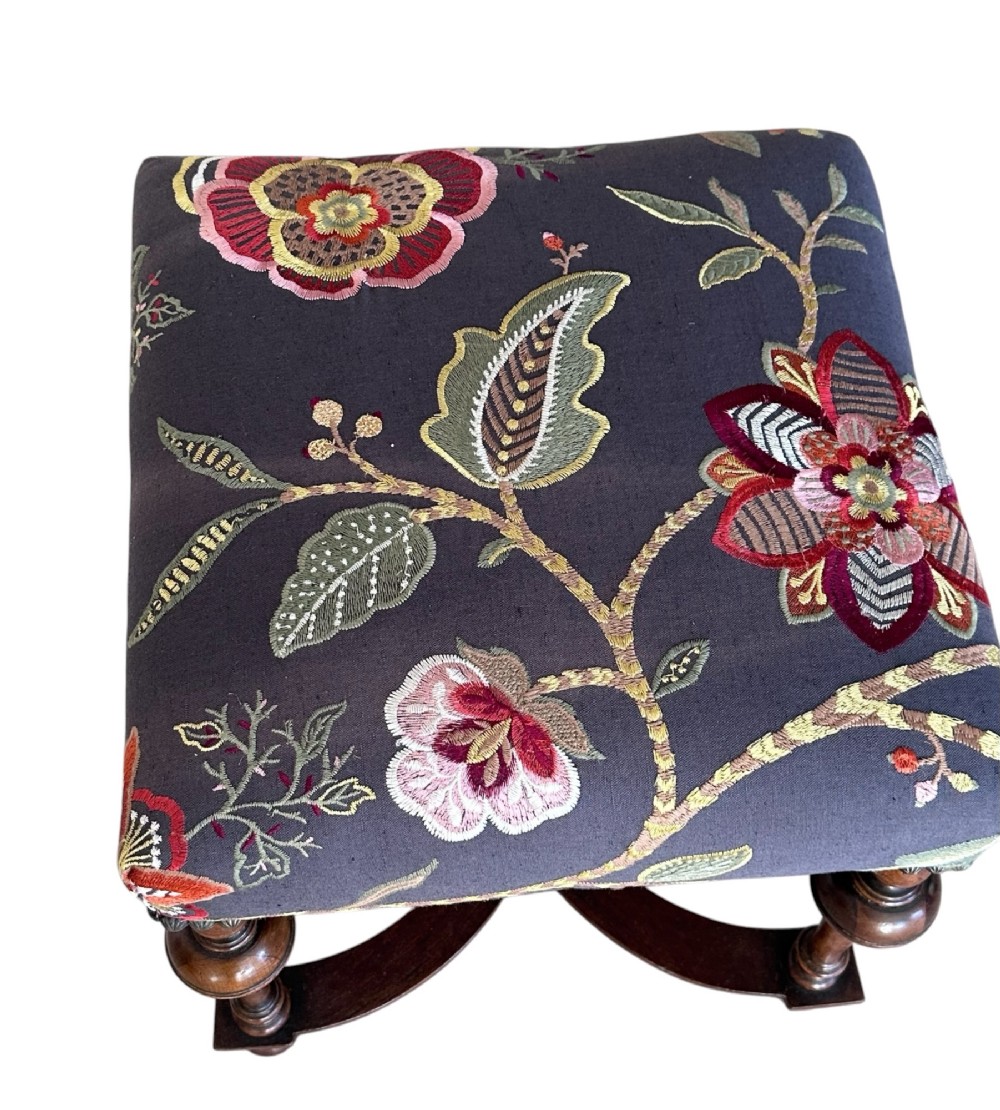 A 19th-century William and Mary style walnut stool featuring turned legs, a curved X-frame stretcher, and dark upholstered top embroidered with colourful floral motifs. View IV