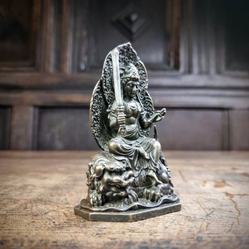 A small 19th-century patinated bronze figure depicting a deity seated upon a mythical lion with an openwork mandorla backdrop. View III