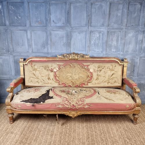 A 19th-century giltwood settee featuring detailed frame carvings, padded armrests, and distressed floral tapestry upholstery. View IV