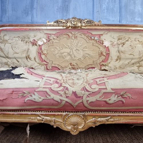 A 19th-century giltwood settee featuring detailed frame carvings, padded armrests, and distressed floral tapestry upholstery. View VII