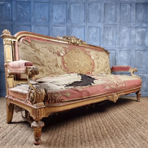 A 19th-century giltwood settee featuring detailed frame carvings, padded armrests, and distressed floral tapestry upholstery. View VIII