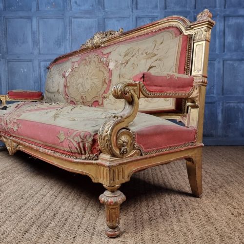 A 19th-century giltwood settee featuring detailed frame carvings, padded armrests, and distressed floral tapestry upholstery. View XI