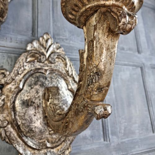 A pair of 17th-century carved wood wall sconces with silvered gilding, featuring ornate cartouche backplates, scrolling arms, and iron prickets. View VI