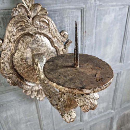 A pair of 17th-century carved wood wall sconces with silvered gilding, featuring ornate cartouche backplates, scrolling arms, and iron prickets. View VIII