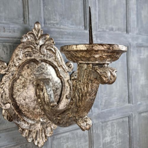 A pair of 17th-century carved wood wall sconces with silvered gilding, featuring ornate cartouche backplates, scrolling arms, and iron prickets. View IX