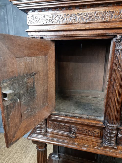 A dark carved oak cupboard featuring two relief-carved doors with figure motifs, upper drawers with ring handles, fluted columns, and an open lower tier. View VI