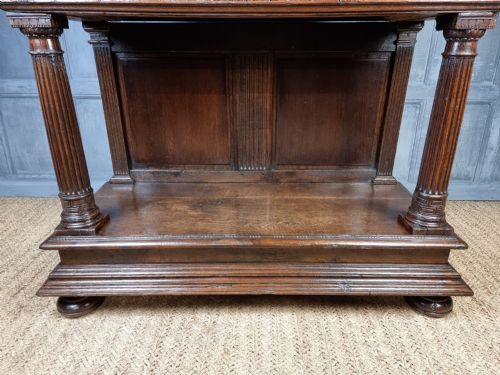 A dark carved oak cupboard featuring two relief-carved doors with figure motifs, upper drawers with ring handles, fluted columns, and an open lower tier. View IX