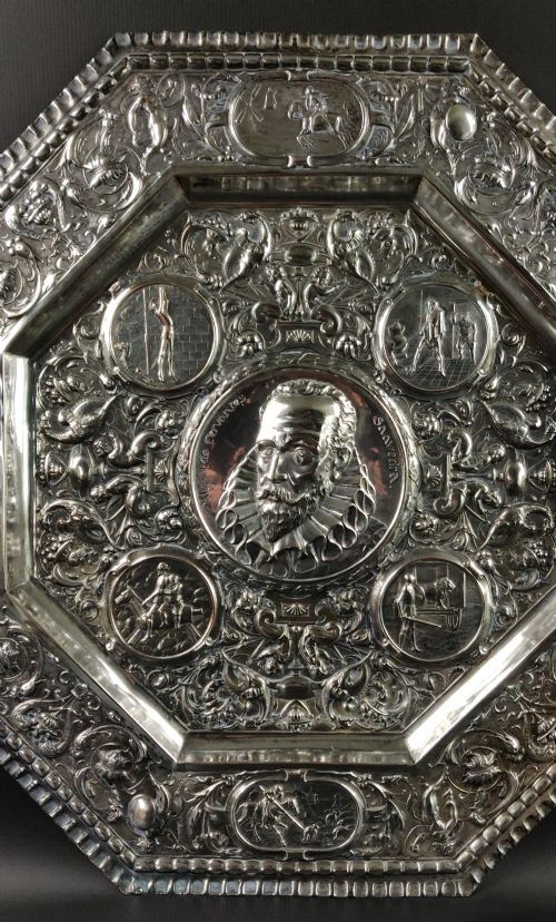 fig 1. An octagonal nineteenth-century silvered metal charger featuring relief repousse decoration depicting a central portrait bust of Miguel de Cervantes surrounded by narrative vignettes and foliate scrollwork.