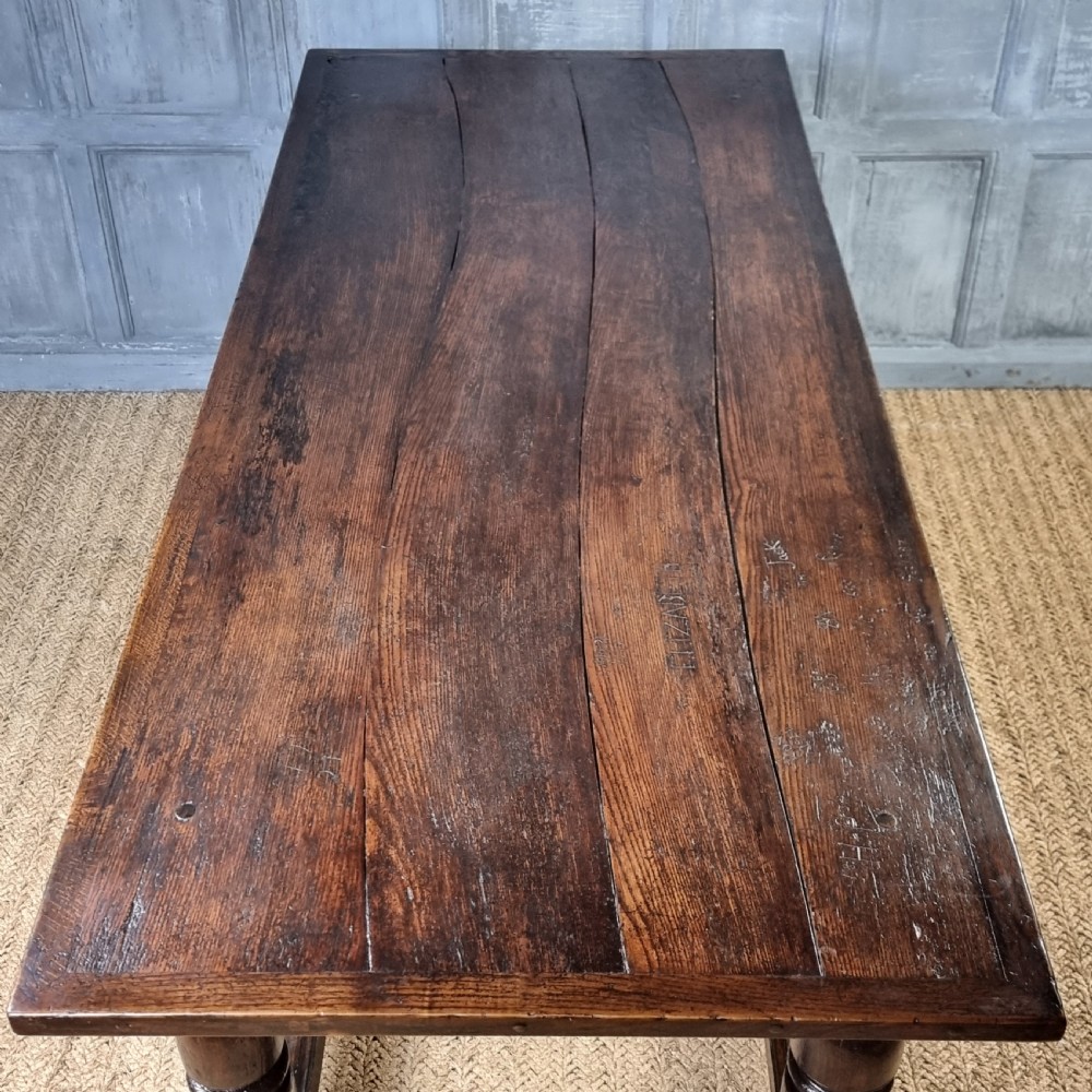 A long dark oak 17th century refectory table featuring a carved frieze along the apron, turned legs, and a sturdy low stretcher base. View XI
