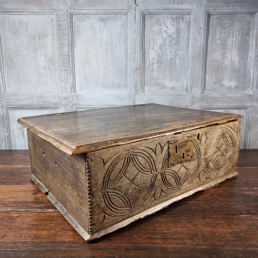 A rectangular 17th century carved oak table box with a flat hinged lid, relief carved geometric front panel, and a centrally mounted iron lock plate. View VI