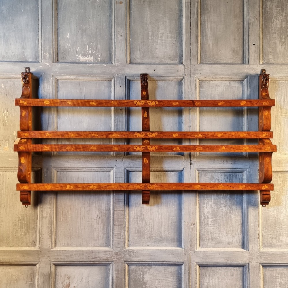 A wall-mounted 19th-century wooden delft rack featuring horizontal plate rails decorated with floral marquetry inlays. View II