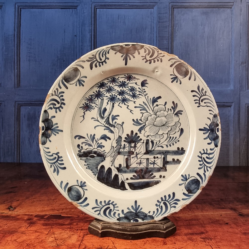 A circular 18th-century tin-glazed earthenware delft charger featuring hand-painted cobalt blue chinoiserie landscape motifs and a decorated rim.
