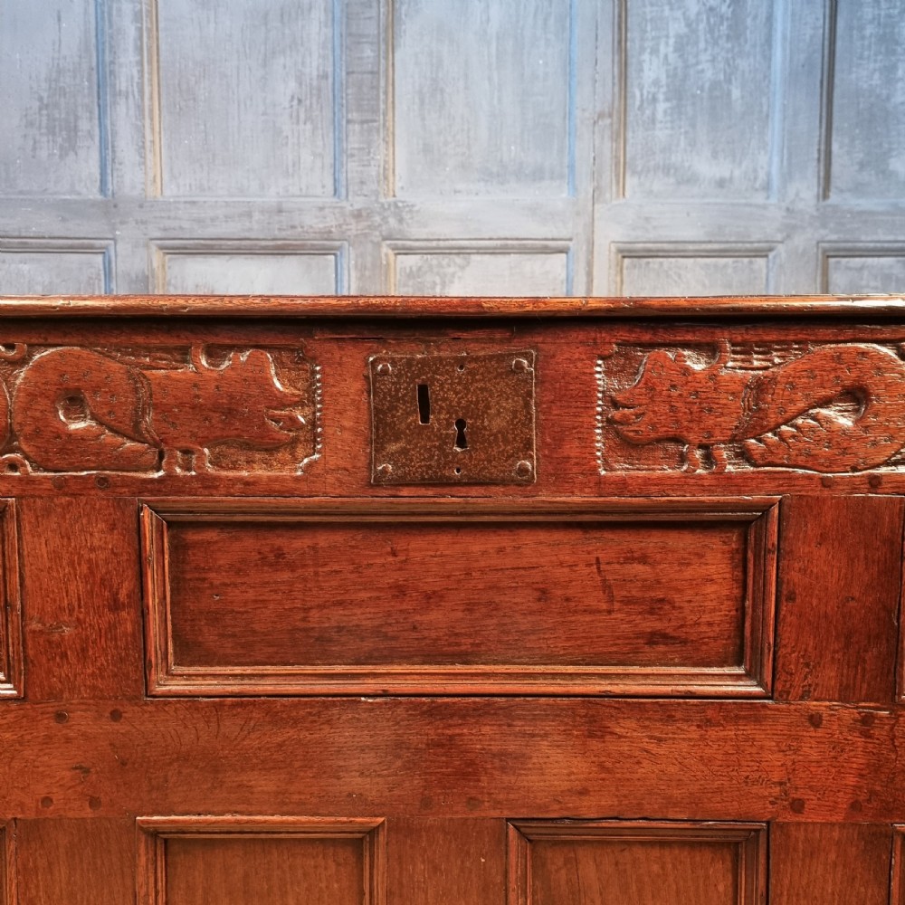 A large 17th-century dark oak coffer featuring hand-carved frieze panels, raised lower panelling, and a central iron lock plate. View II