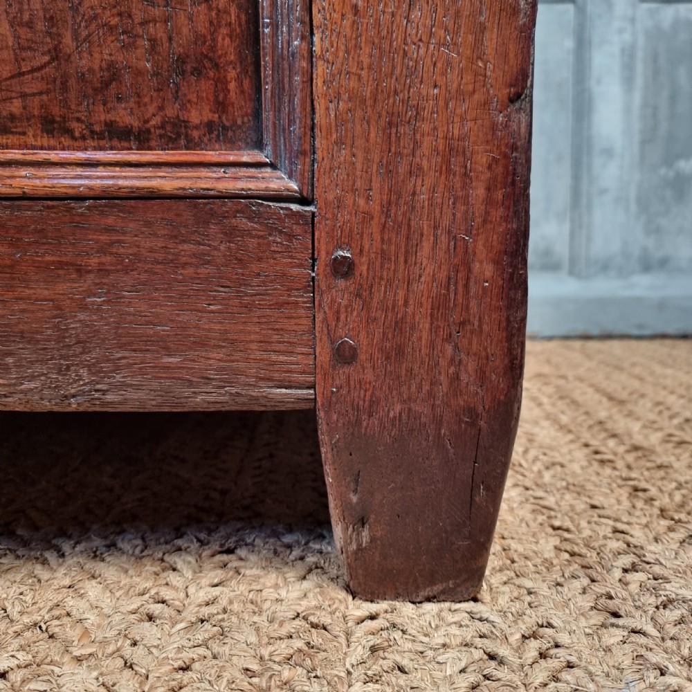 A large 17th-century dark oak coffer featuring hand-carved frieze panels, raised lower panelling, and a central iron lock plate. View V