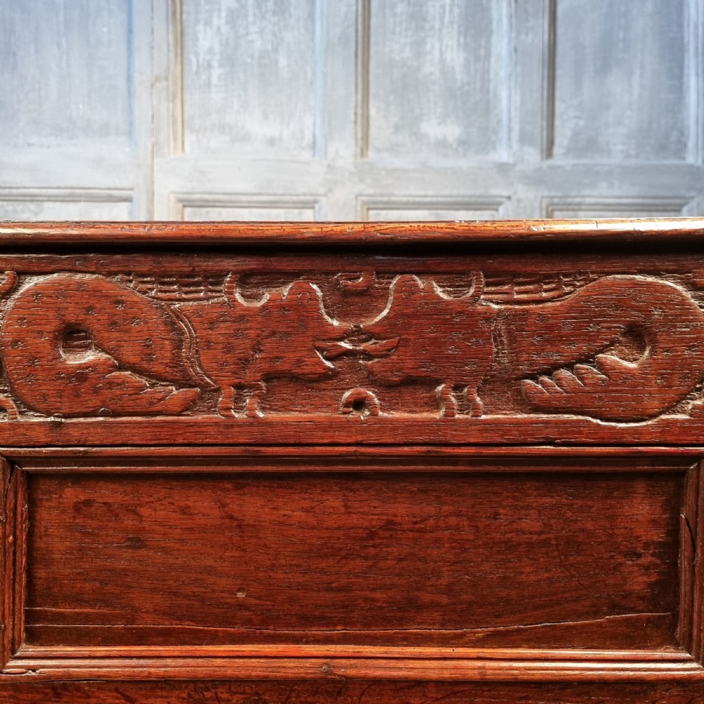A large 17th-century dark oak coffer featuring hand-carved frieze panels, raised lower panelling, and a central iron lock plate. View VIII