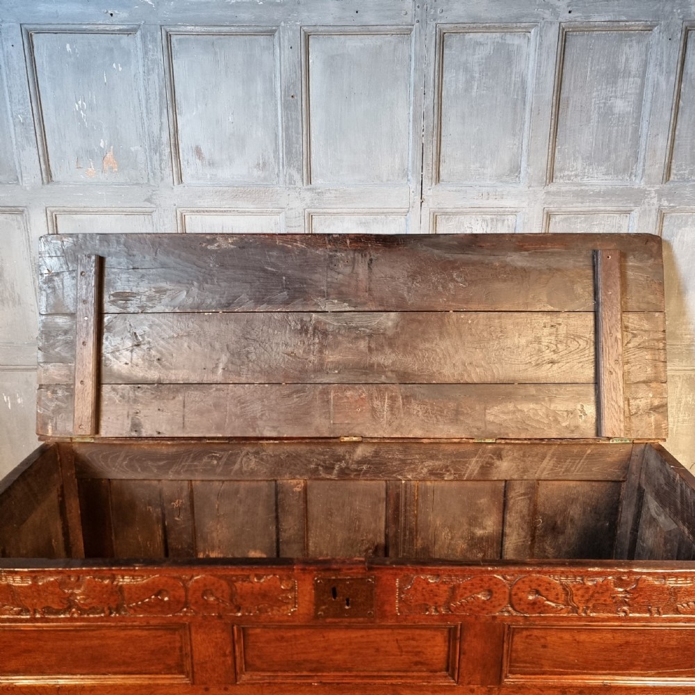 A large 17th-century dark oak coffer featuring hand-carved frieze panels, raised lower panelling, and a central iron lock plate. View XII