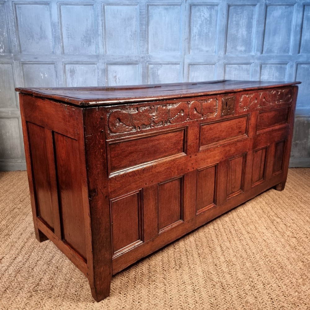 A large 17th-century dark oak coffer featuring hand-carved frieze panels, raised lower panelling, and a central iron lock plate. View XV