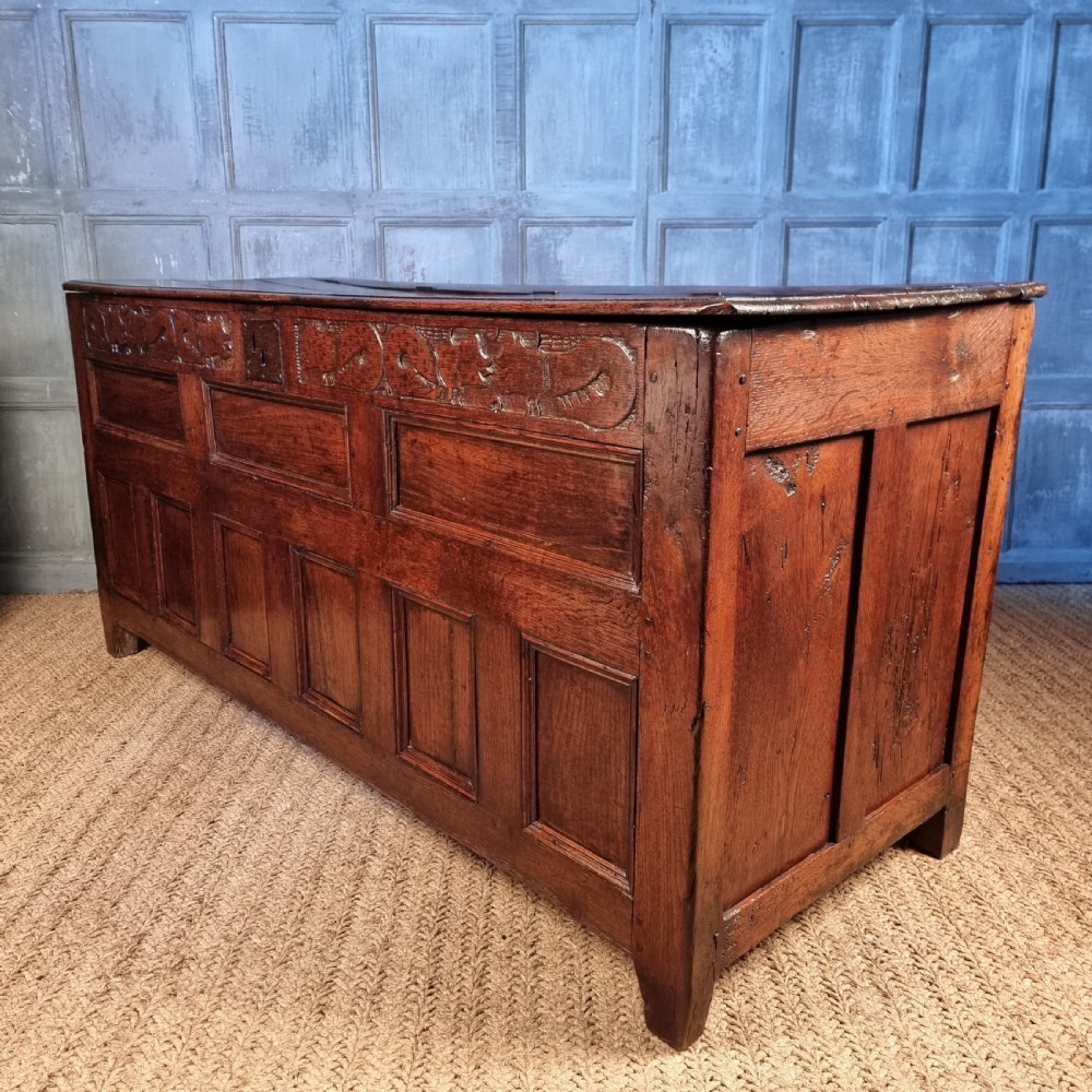 A large 17th-century dark oak coffer featuring hand-carved frieze panels, raised lower panelling, and a central iron lock plate. View XVII