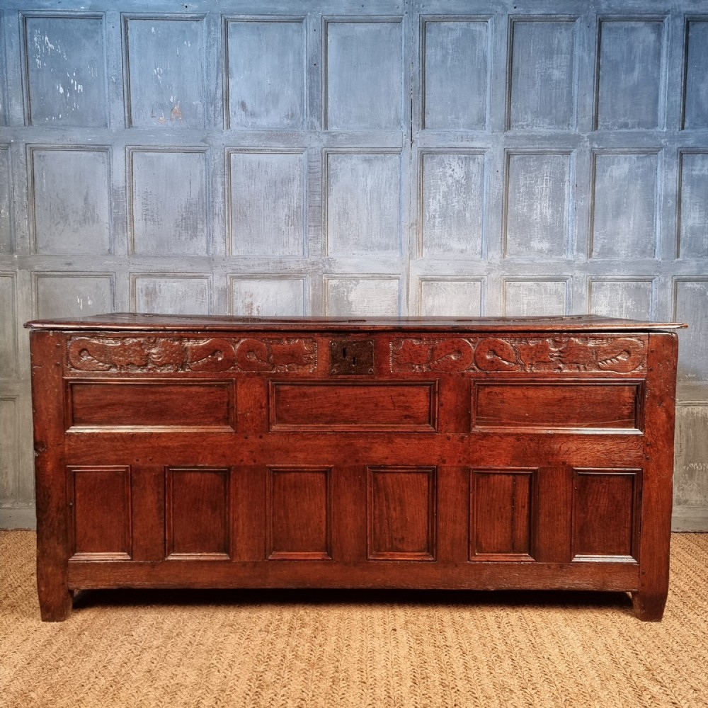 A large 17th-century dark oak coffer featuring hand-carved frieze panels, raised lower panelling, and a central iron lock plate.