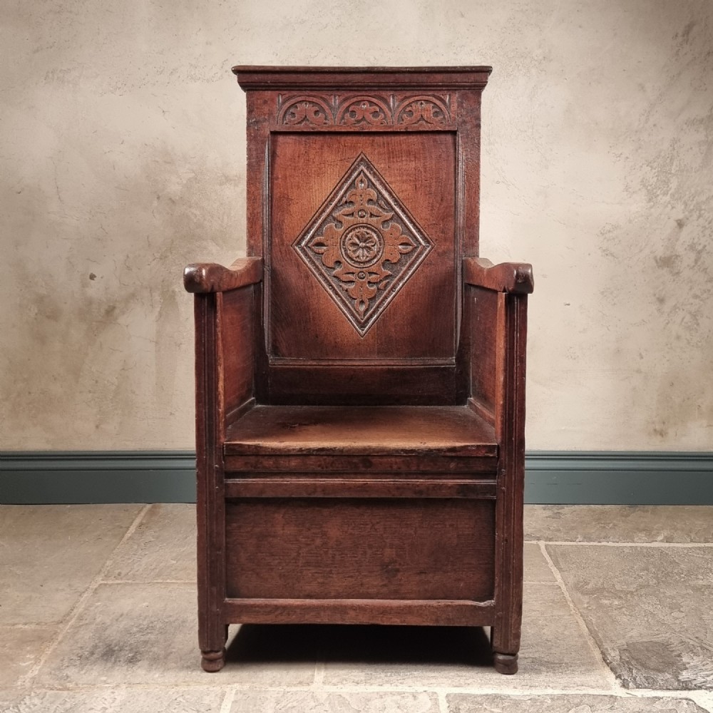 A 17th-century carved dark oak armchair featuring a high back with a central diamond lozenge motif, arcaded carving, and an enclosed box base.
