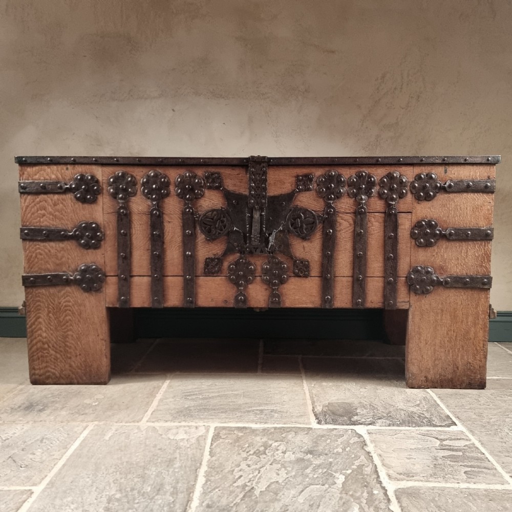 A heavy 16th-century oak coffer featuring wrought-iron strapwork, rosette rivets, and a large central iron lockplate set on wide timber stiles. View IV