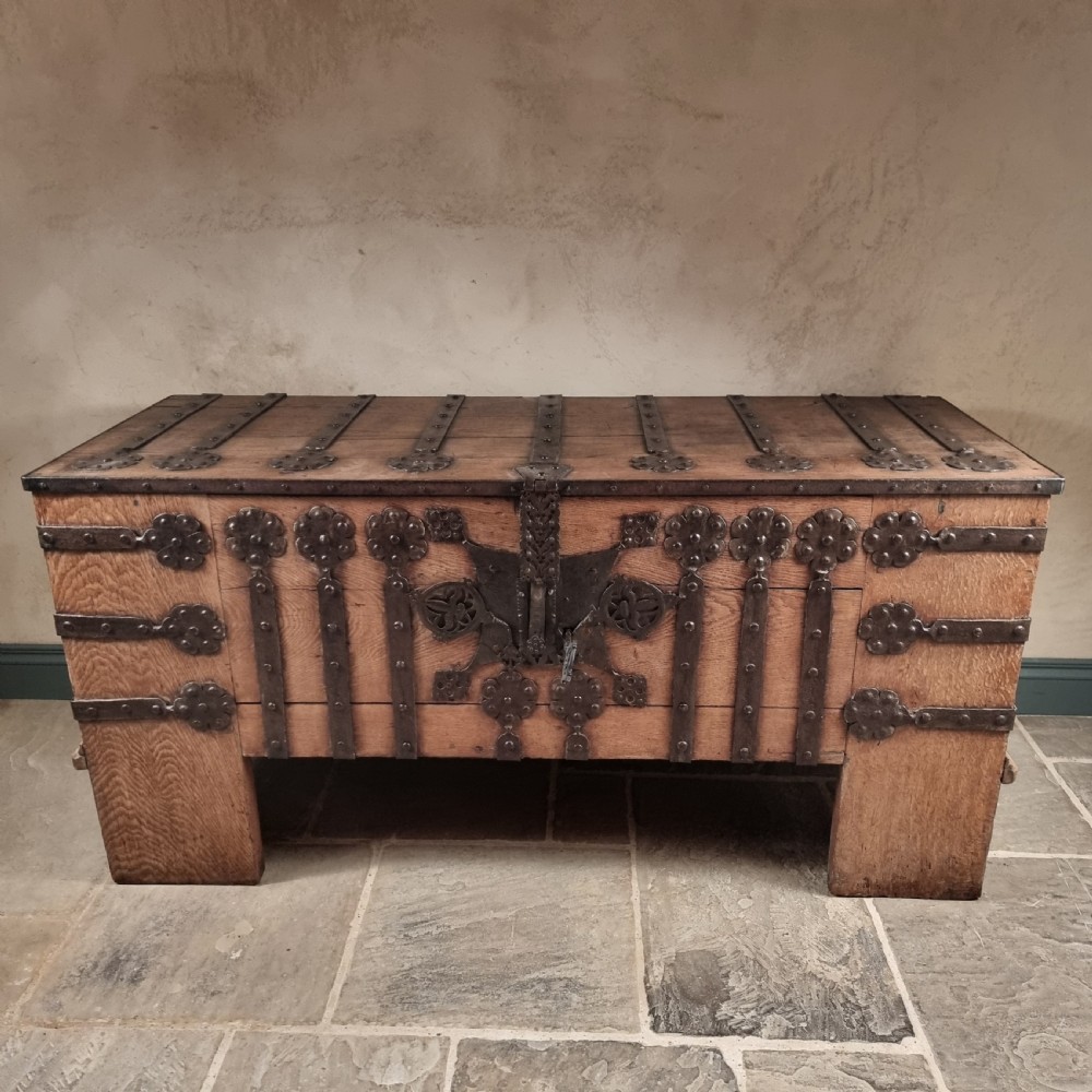 A heavy 16th-century oak coffer featuring wrought-iron strapwork, rosette rivets, and a large central iron lockplate set on wide timber stiles. View V