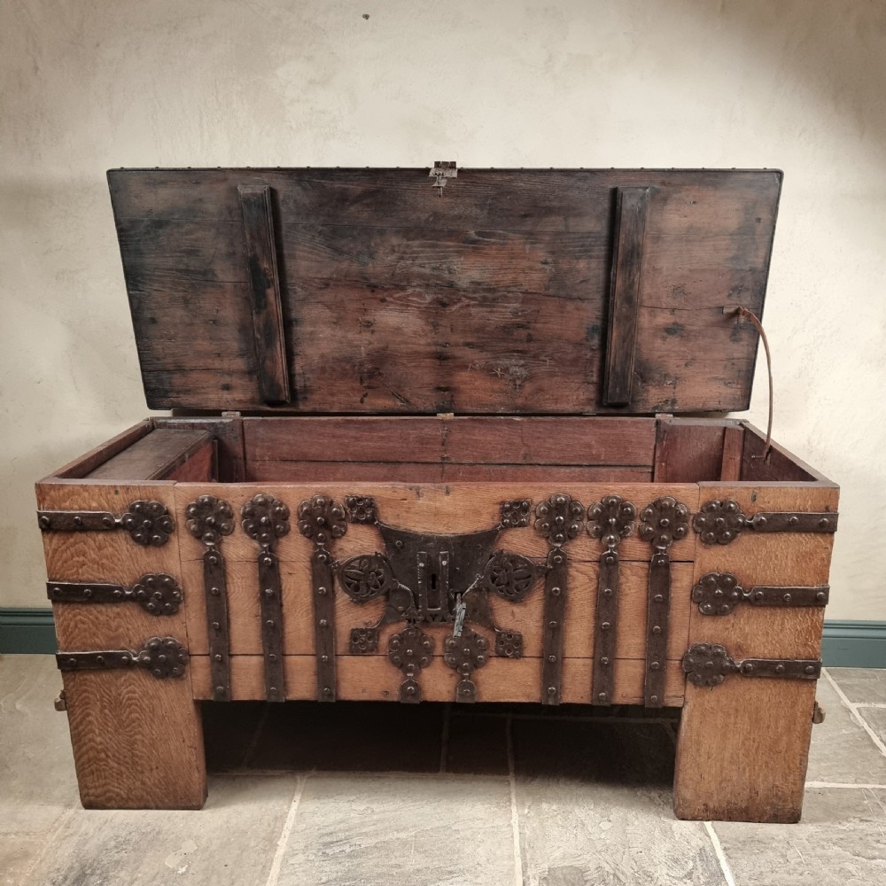 A heavy 16th-century oak coffer featuring wrought-iron strapwork, rosette rivets, and a large central iron lockplate set on wide timber stiles. View IX