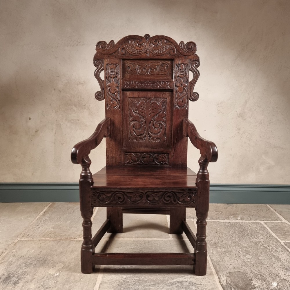 A dark carved oak seventeenth-century wainscot armchair featuring a panelled backrest, scrolling ears, turned front legs, and square stretchers.