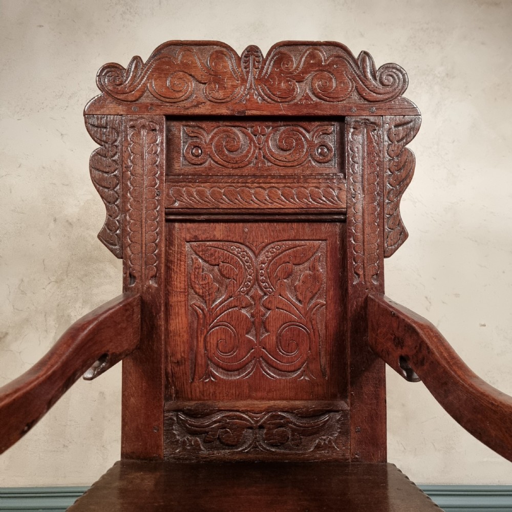 A dark carved oak seventeenth-century wainscot armchair featuring a panelled backrest, scrolling ears, turned front legs, and square stretchers. View II