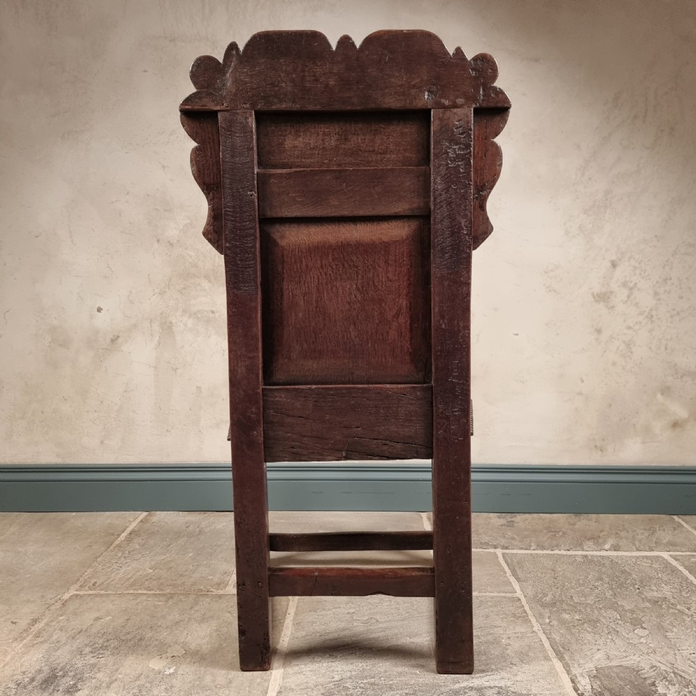 A dark carved oak seventeenth-century wainscot armchair featuring a panelled backrest, scrolling ears, turned front legs, and square stretchers. View VII