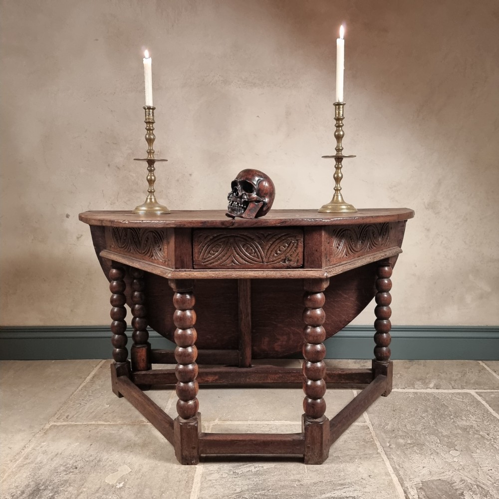 A 17th century dark oak credence table featuring a semi-octagonal top, carved lunette frieze, and bobbin-turned legs with lower stretchers.