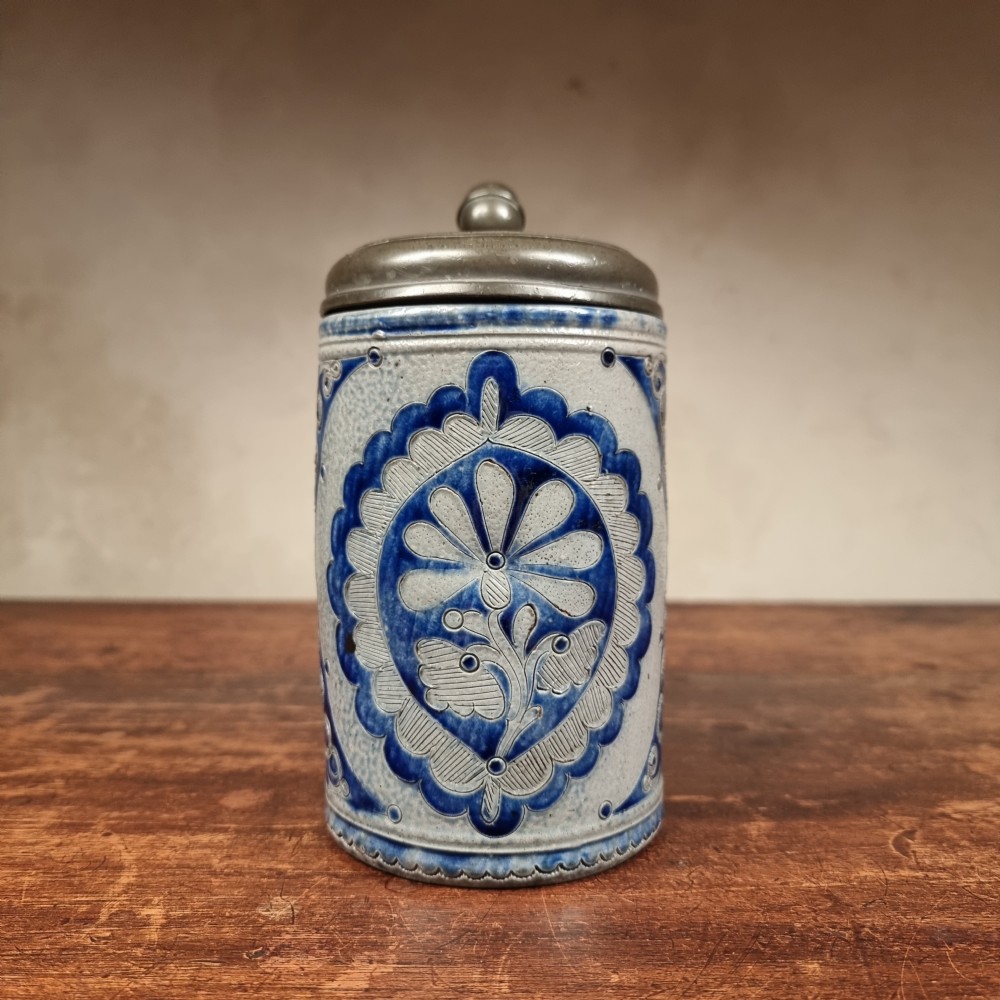 An 18th-century cylindrical salt-glazed stoneware tankard featuring grey clay, hand-painted cobalt blue incised decorations, and a hinged pewter lid with a ball thumblift. View II