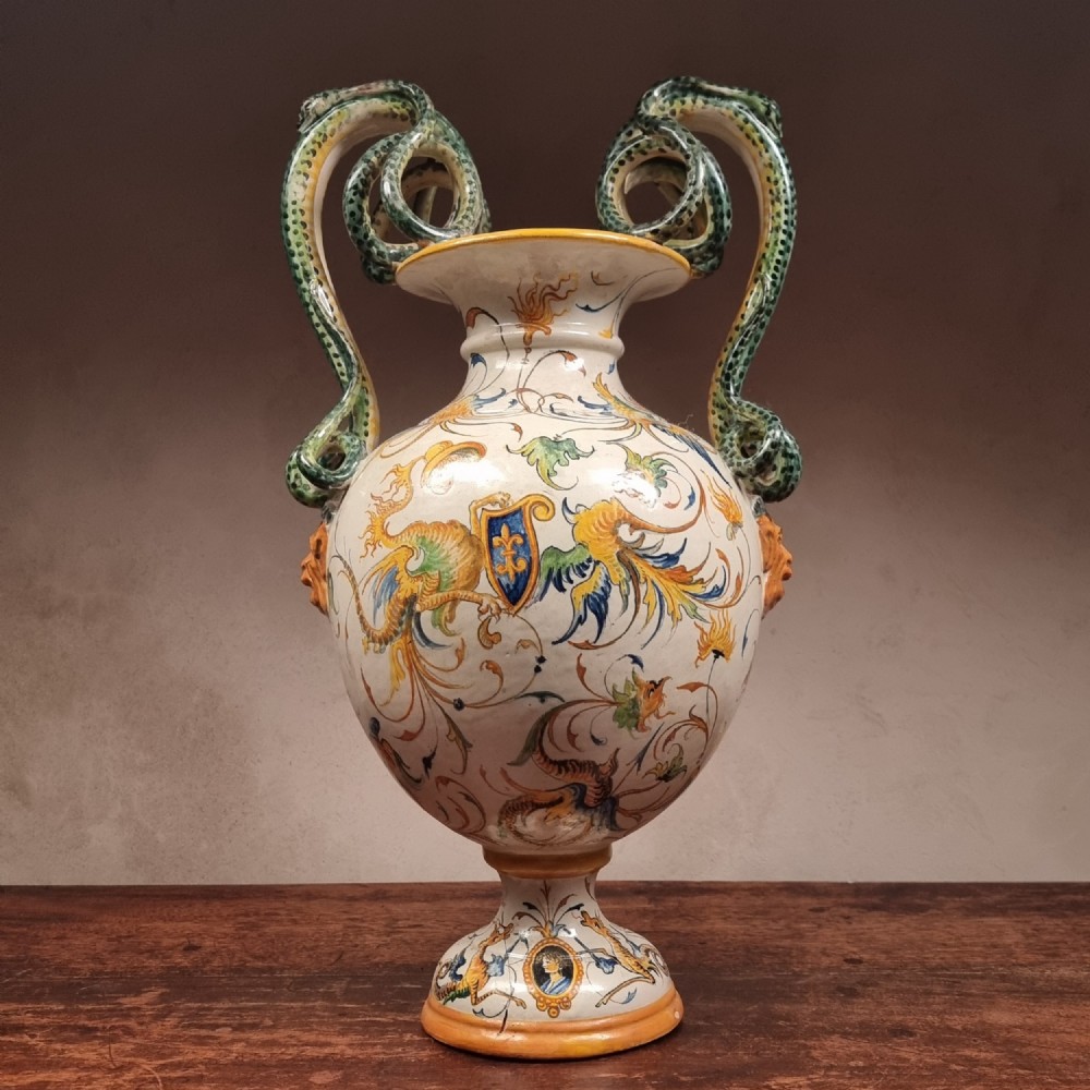 A 19th-century Italian majolica urn vase featuring hand-painted mythological grotesques, a coat of arms, and twin green serpent-formed handles.