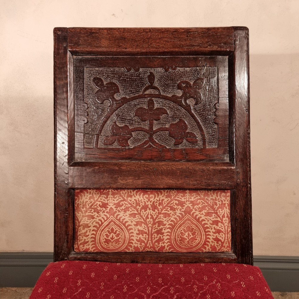 A dark carved oak side chair with an arched floral back panel, red upholstered lumbar cushion, red seat, and turned front legs. View VI
