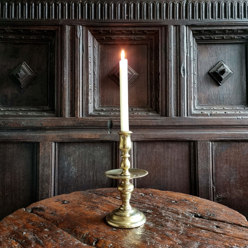 An antique cast brass Heemskerk candlestick featuring a baluster turned stem, a prominent central drip pan, and a wide domed base.