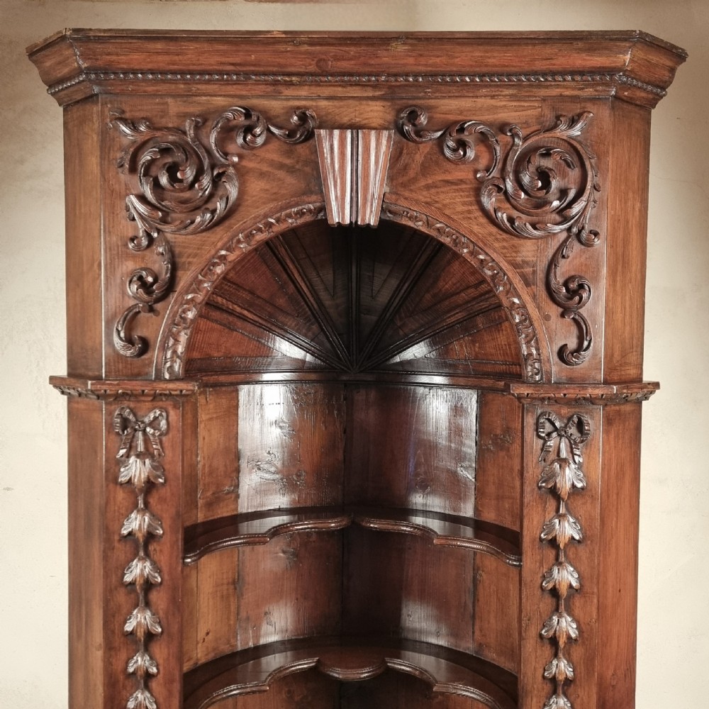 A tall dark mahogany corner cupboard featuring an open carved arched alcove with shaped shelves above a two-door lower cupboard. View II